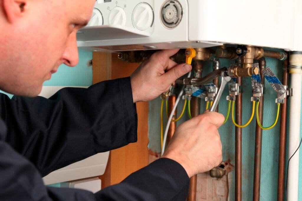 Heating engineer adjusting copper pipes below a boiler with tools in hand.