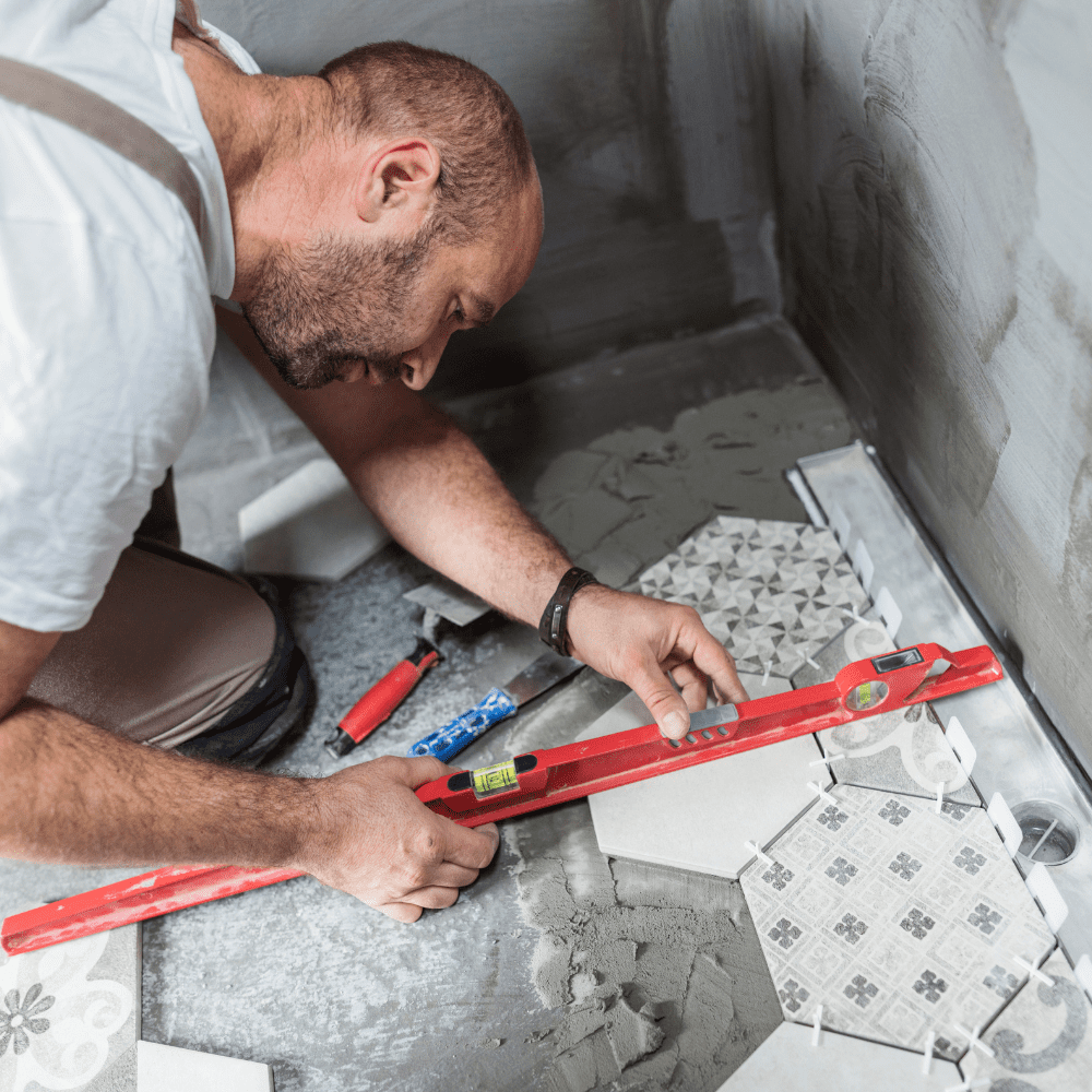 Tradesman using a red spirit level while fitting patterned floor tiles with adhesive.