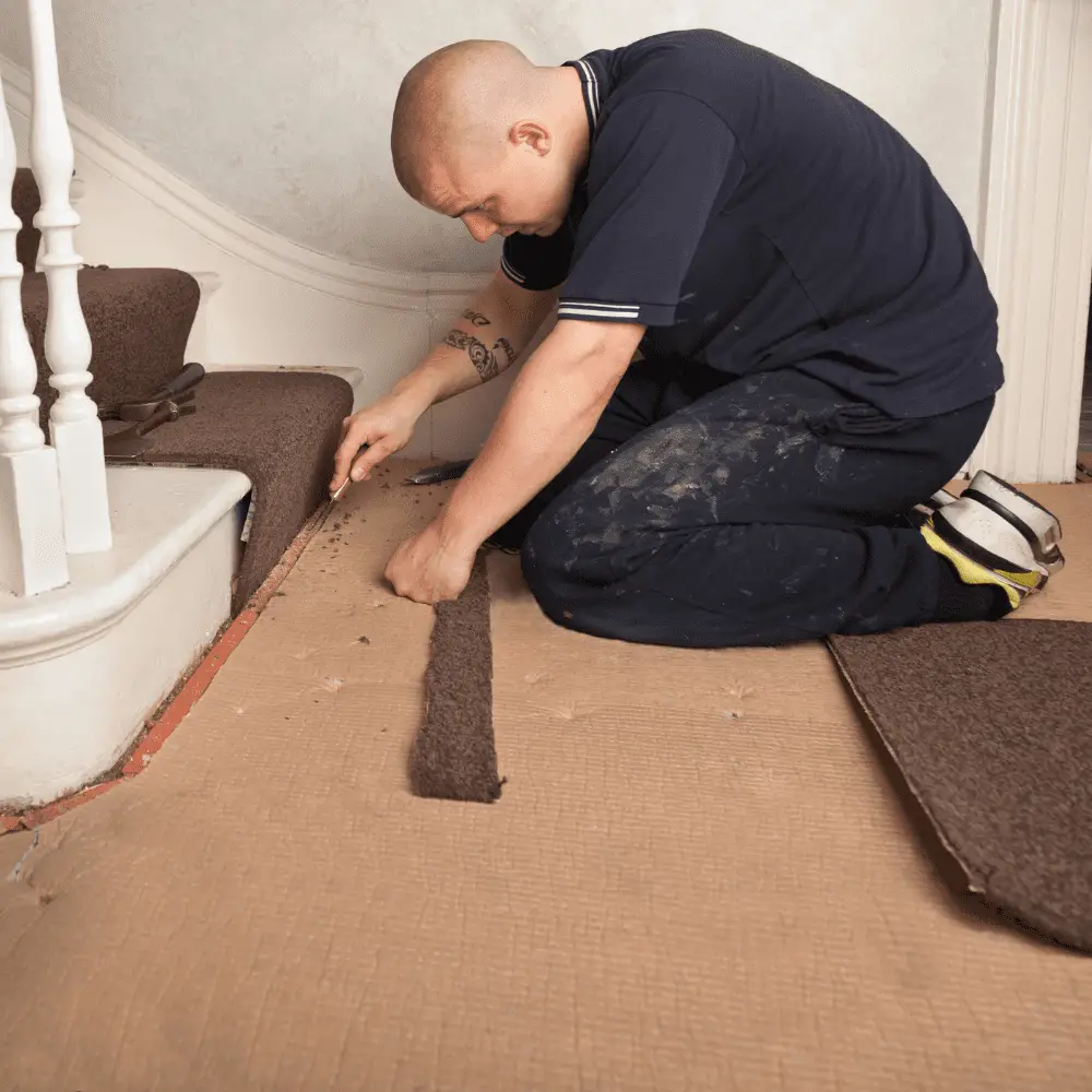 Flooring fitter installing carpet on stairs with tools.