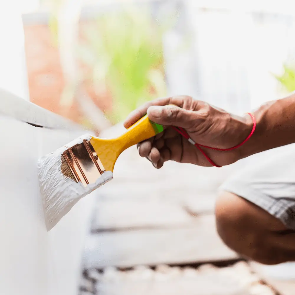 Decorator painting exterior wall with white paint and brush.