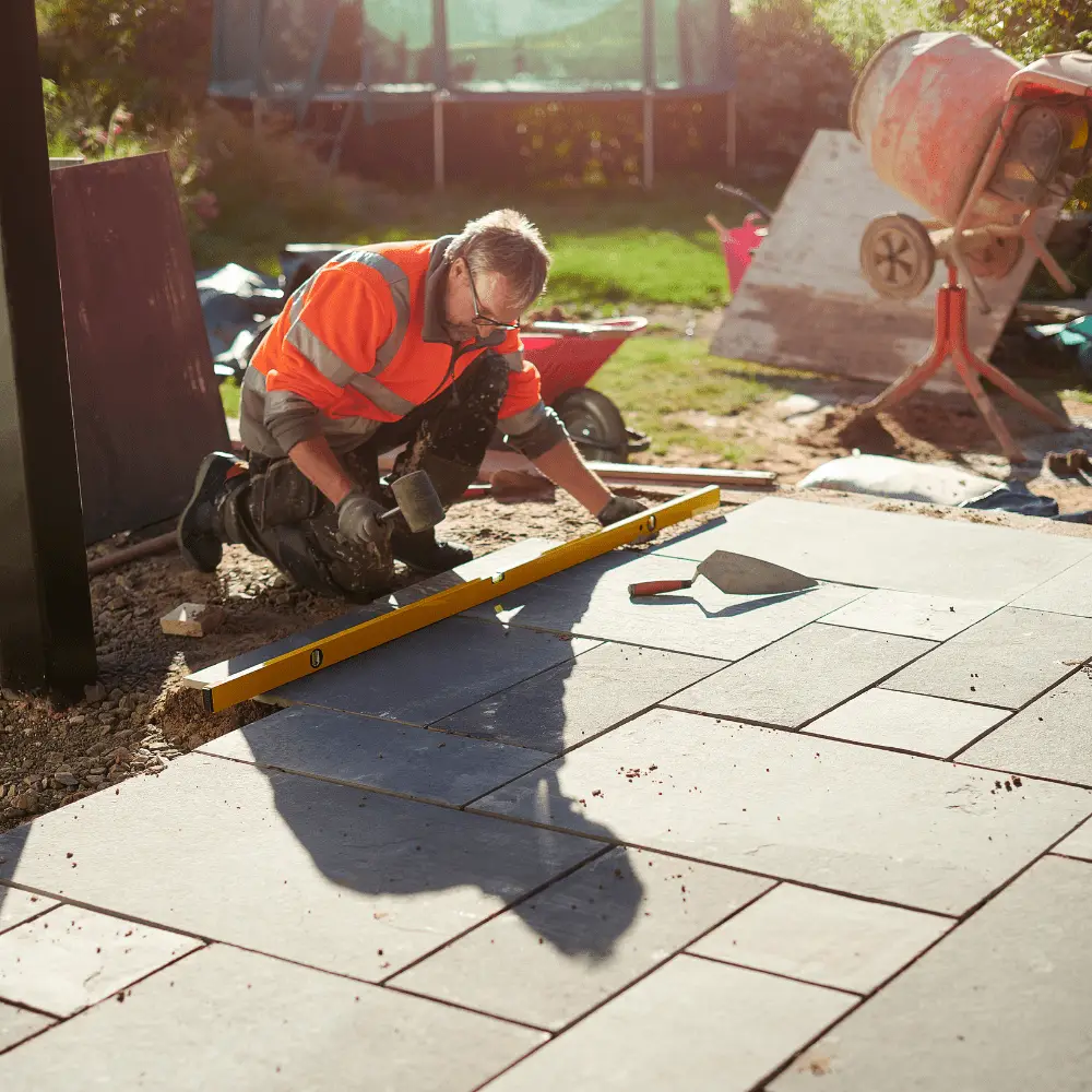 Landscaper laying paving slabs with level and tools.