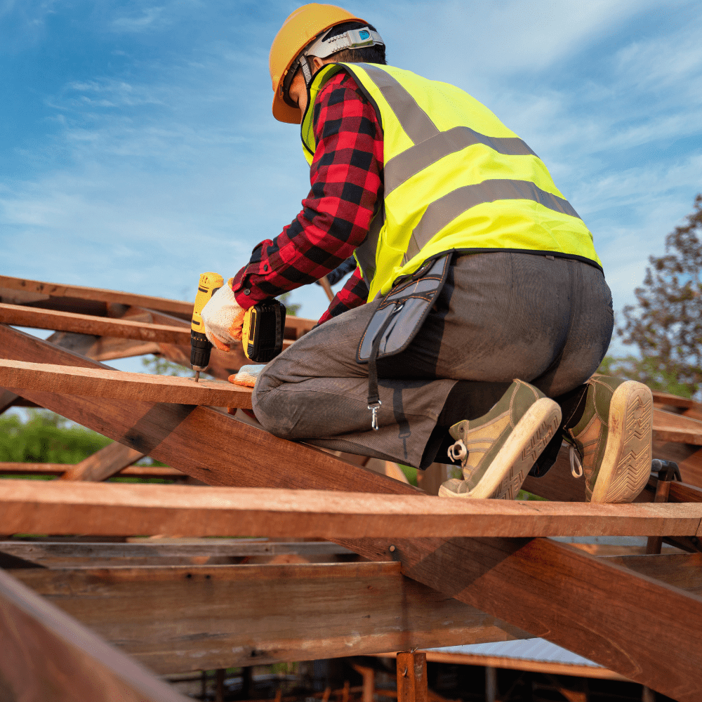 Roofer drilling timber beams on pitched roof frame.