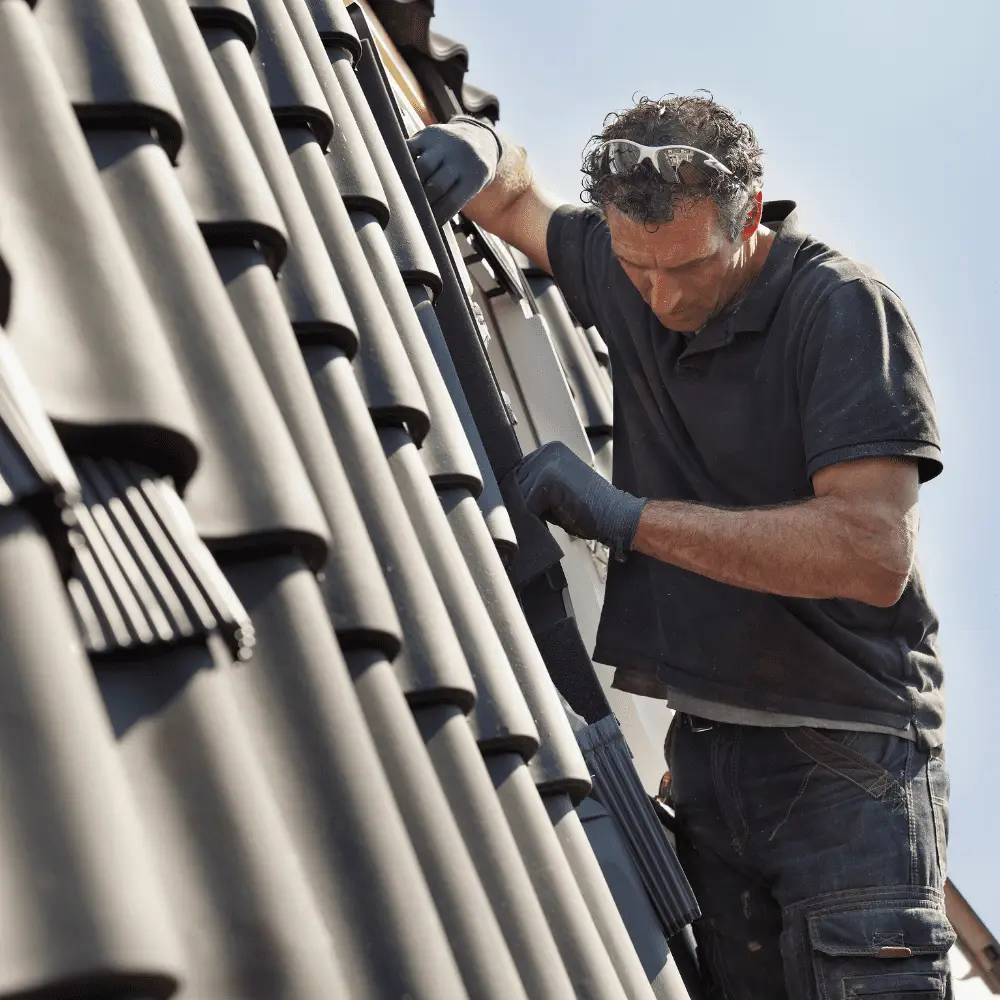 Roofer installing black tiles on a sloped roof.