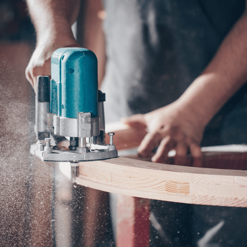 Joiner using a router to cut curved wood edge in a workshop.